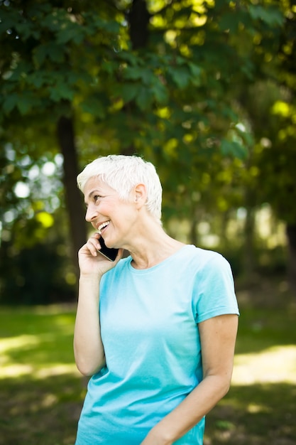 Sportive femme âgée à l'aide de téléphone portable dans le parc