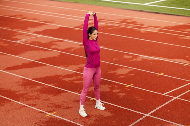 Une sportive en forme étire les bras et se prépare à courir au stade.