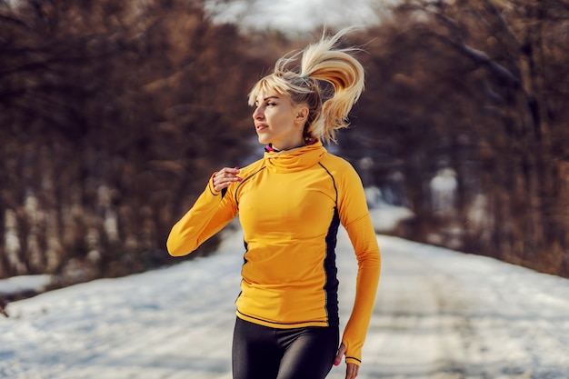 Sportive en forme fonctionnant dans la forêt au jour d'hiver enneigé. Fitness hivernal, exercices cardio, temps froid