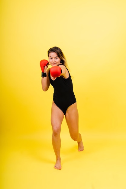 Sportive forte dans des gants de boxe préparé coup de pied haut isolé sur fond jaune rouge blanc