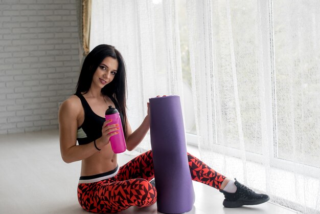 Sportive jeune fille avec un tapis de fitness et une bouteille d'eau. Mode de vie sain.