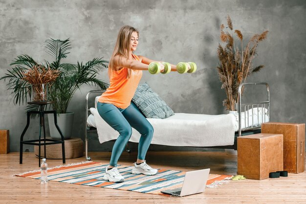 Photo une sportive joyeuse aux cheveux blonds fait un squat avec des haltères dans la chambre à coucher.