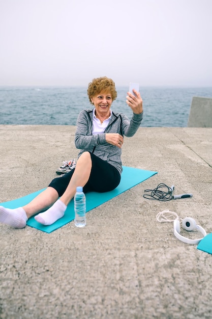 Sportive senior prenant selfie par la jetée de la mer