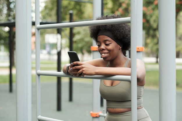 Sportive souriante envoyant des SMS dans un smartphone par des installations