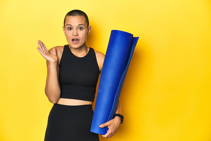 Photo sportive tenant un tapis de yoga fond de studio jaune surpris et choqué