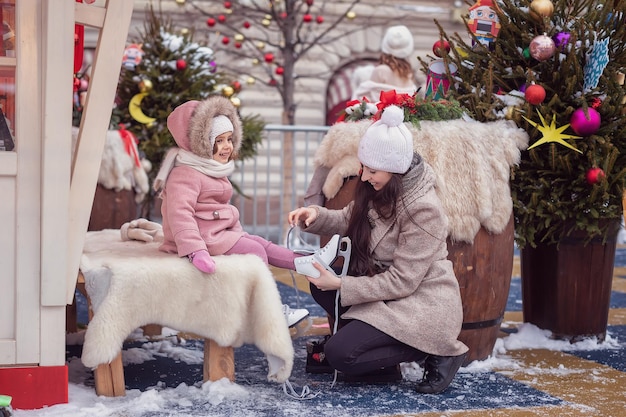 Sports d'hiver en famille dans le parc Maman aide sa petite fille à mettre des patins Fond de Noël Concept de vacances de Noël et d'hiver en famille
