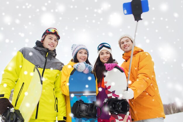 sports d'hiver, loisirs, amitié, technologie et concept de personnes - amis heureux avec snowboards et smartphone prenant selfie