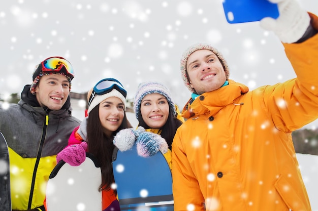 Photo sports d'hiver, loisirs, amitié, technologie et concept de personnes - amis heureux avec snowboards et smartphone prenant selfie