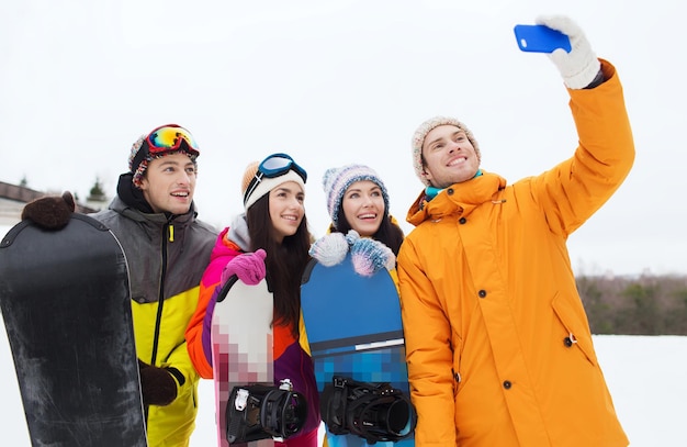 sports d'hiver, loisirs, amitié, technologie et concept de personnes - amis heureux avec snowboards et smartphone prenant selfie