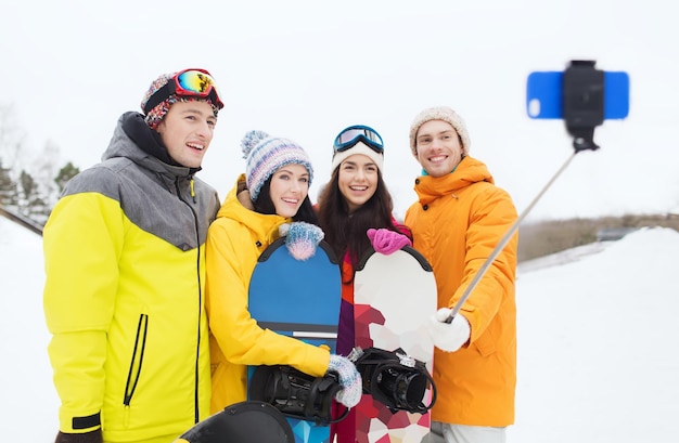 sports d'hiver, loisirs, amitié, technologie et concept de personnes - amis heureux avec snowboards et smartphone prenant selfie