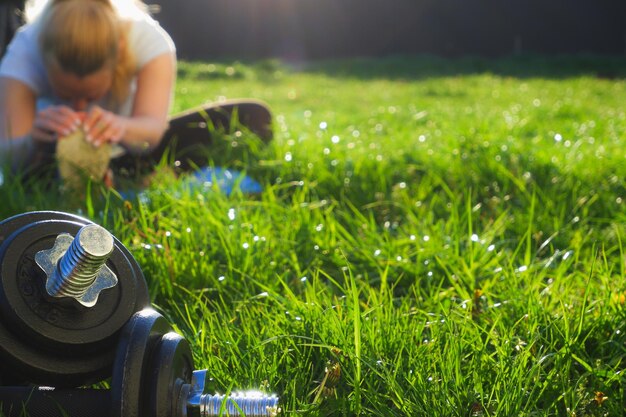 Les sports en plein air, les haltères sur l'herbe verte à la lumière du soleil couchant, la femme au fond s'étire après un entraînement intensif.