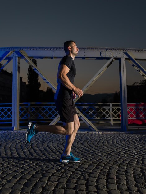 sports urbains, jeune homme en bonne santé faisant du jogging sur le pont de la ville tôt le matin dans la nuit