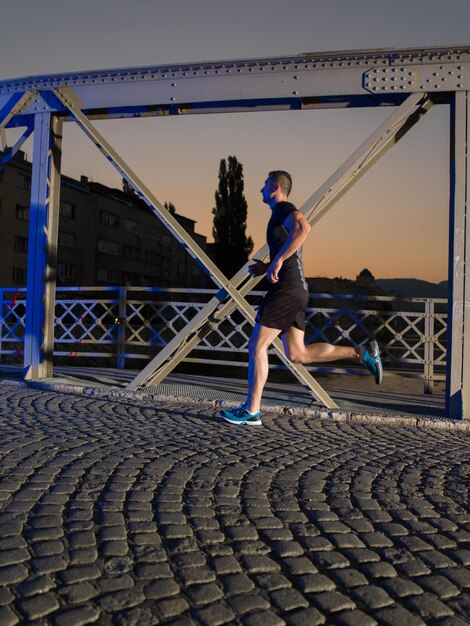 sports urbains, jeune homme en bonne santé faisant du jogging sur le pont de la ville tôt le matin dans la nuit