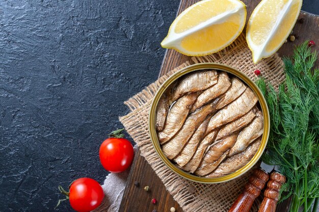 Sprats de poisson de fruits de mer en conserve de la Baltique dans une boîte de conserve sur fond noir avec espace de copie. Vue de dessus, mise à plat.