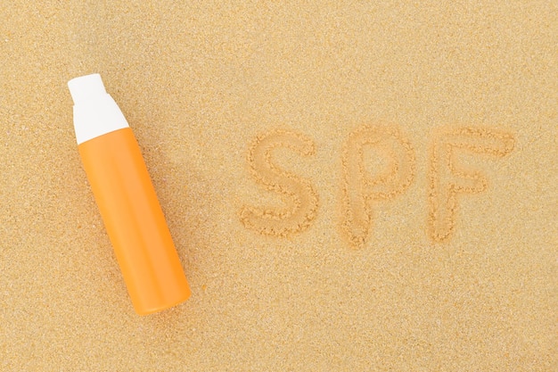 Spray solaire en bouteille orange et inscription sur le sable SPF