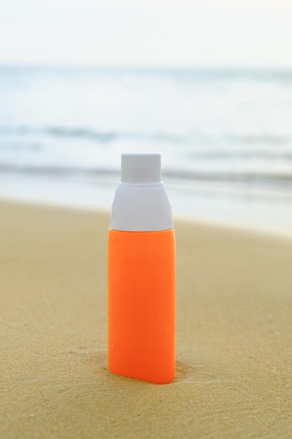 Spray solaire en bouteille orange sur le sable sur fond de vagues de la mer