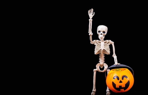 Photo un squelette humain agite une citrouille orange d'halloween sur un fond noir.