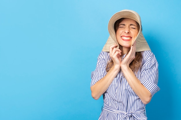 Squint jeune fille au chapeau et robe sur un mur bleu. Concept de faire des souhaits, de repos et de voyage