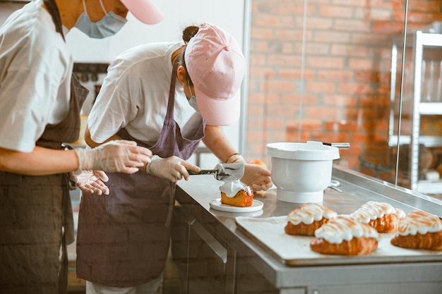 Une stagiaire en confiserie étale de la crème sur une génoise pendant qu'une collègue lui apprend à la boulangerie