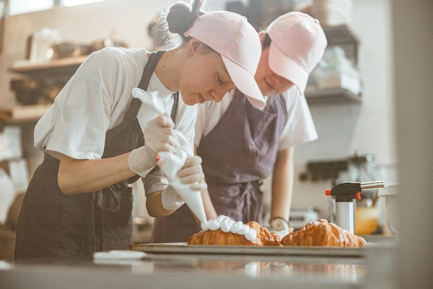 Photo un stagiaire confiseur applique de la crème sur un croissant sous le contrôle d'un collègue qualifié dans une boulangerie