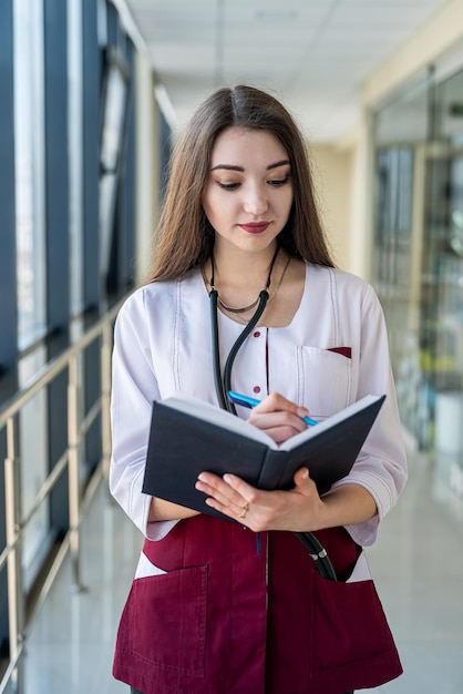 Stagiaire fille se tient en clinique avec stéthoscope et notes Concept de médecine