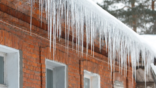 Stalactite de glace accrochée au toit avec mur de briques rouges