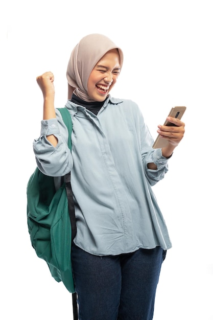 Stand d'étudiante voilée excité à l'aide de téléphone avec sac à dos en arrière-plan isolé