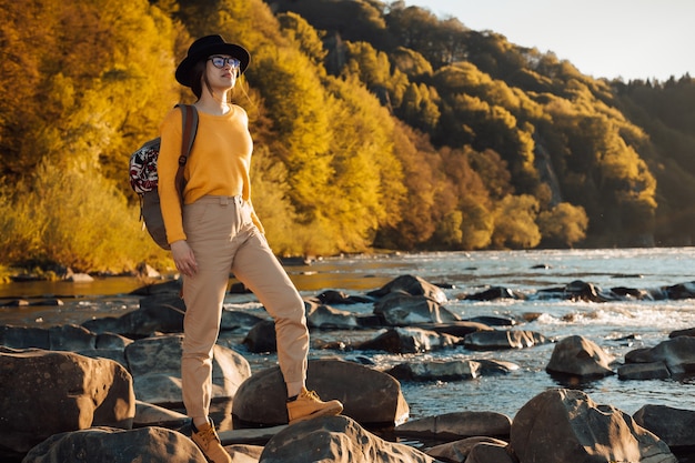 Stand de voyageur de jeune femme avec sac à dos sur fond de nature de la rivière