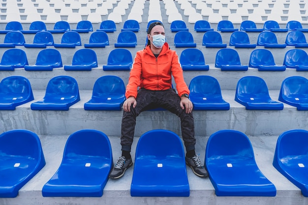 Stands de football avec chaises en plastique bleu. Fan de football avec un masque de protection dans le stade. Compétitions sportives pendant la quarantaine et le verrouillage du coronavirus covid 19.