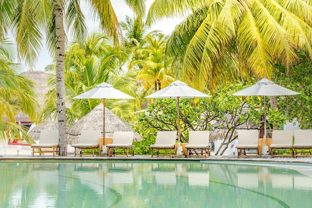 Station balnéaire tropicale avec chaises longues et parasols sous les feuilles de palmier. Vacances d'été