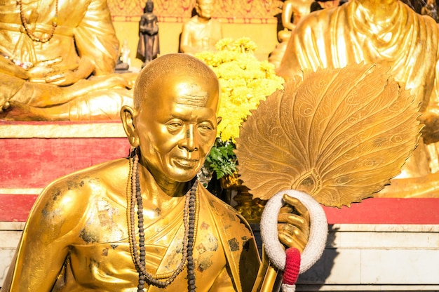 Statue dorée d'un vieux moine bouddhiste avec un anneau de fleurs dans le sanctuaire de Doi Suthep