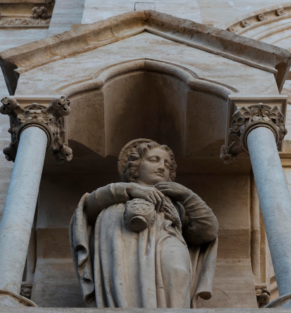 Une statue de femme tenant une bouteille de vin se trouve devant un bâtiment.