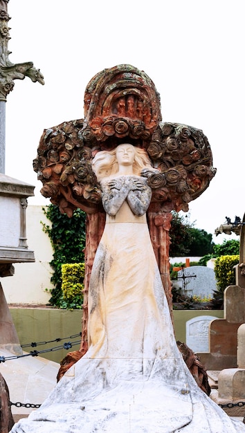Une statue de femme vêtue de blanc se dresse dans un cimetière.