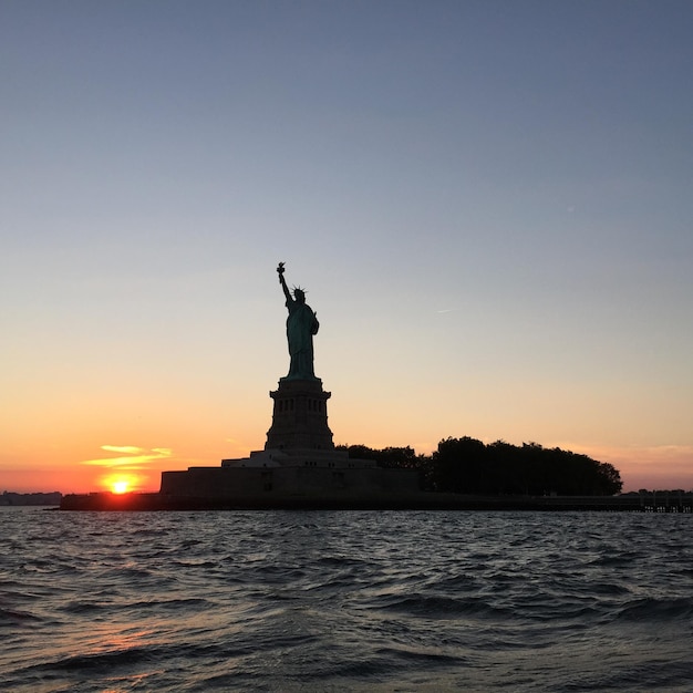 Photo la statue de la liberté au milieu de la mer contre le ciel au coucher du soleil