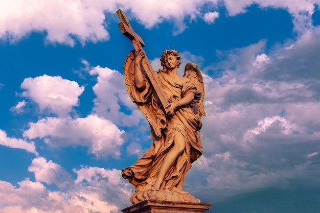 Photo statue en marbre d'ange avec la croix au coucher du soleil, l'un des dix anges sur le pont saint-ange, symboles de la passion du christ, rome, italie