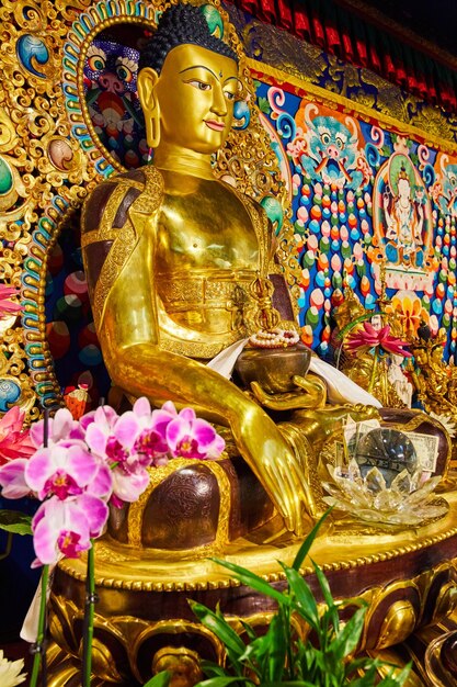 Statue ornée de Bouddha en or dans un sanctuaire avec des orchidées roses