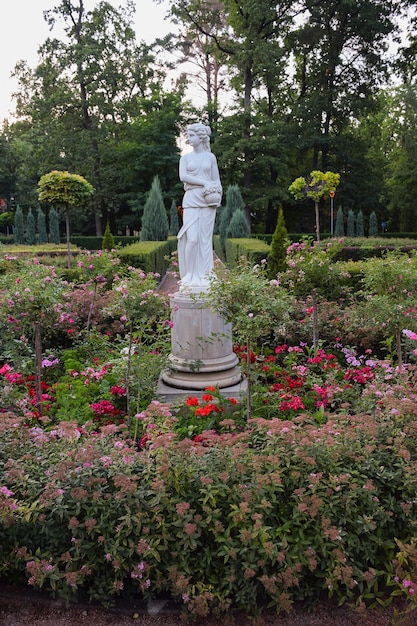 Statue en pierre blanche d'une fille dans un parc d'été, près d'elle il y a beaucoup de fleurs, d'arbres et de verdure