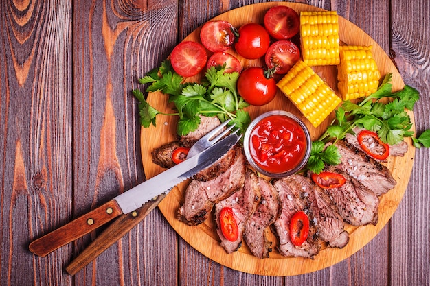 Steak d'agneau BBQ avec légumes et herbes sur bois foncé.