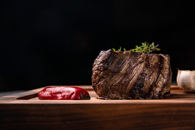 Steak américain juteux sur le plateau avec épices, tomates et légumes grillés. Sur une table noire