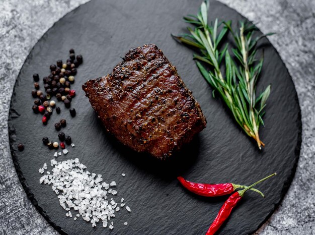 Un steak aux épices et herbes sur une surface en pierre noire.