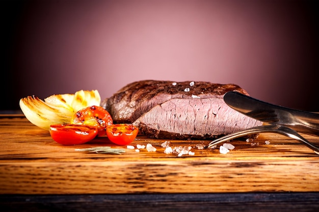 Photo steak aux oignons frits et tomates cerises sur une planche de bois