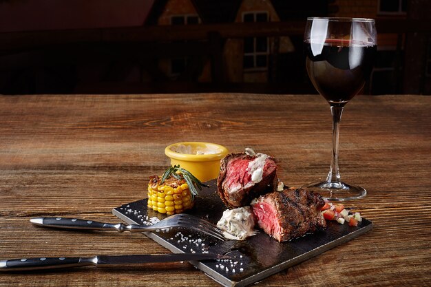 Steak de barbecue avec un verre de vin rouge en gros plan sur un tableau noir sur fond de bois