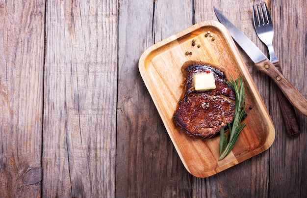 Steak de boeuf au beurre sur une plaque en bois avec du romarin et du poivre, vue du dessus