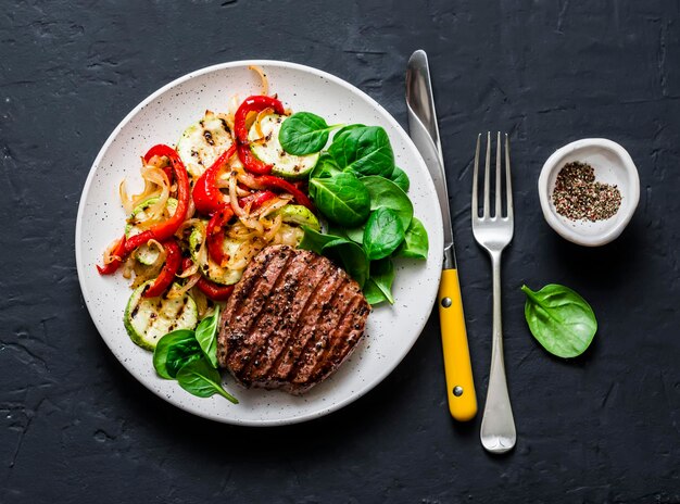 Steak de boeuf aux légumes grillés courgettes poivrons et épinards frais sur fond sombre