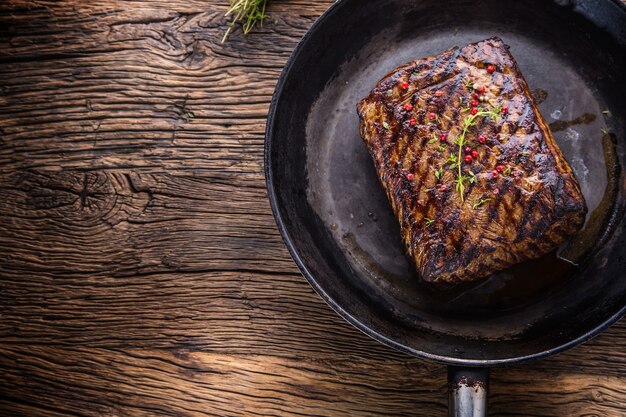 Steak de bœuf. Bifteck de faux-filet juteux dans une poêle sur une planche de bois avec des herbes et du poivre.