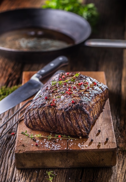 Steak de bœuf. Bifteck de faux-filet juteux dans une poêle sur une planche de bois avec des herbes et du poivre.