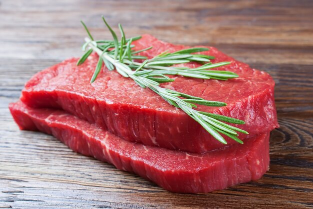 Steak de boeuf cru au romarin sur fond de bois marron