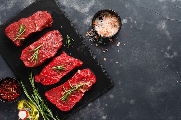 Steak de boeuf cru aux épices, oignons et romarin sur ardoise sombre ou fond de béton. Vue de dessus