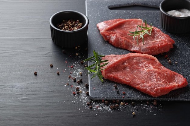 Steak de boeuf cru aux épices sur une planche à découper sombre Espace de copie