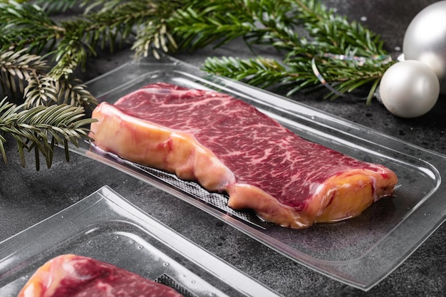 Steak de boeuf cru dans un ensemble emballé sous vide, sur fond de table en pierre noire foncée